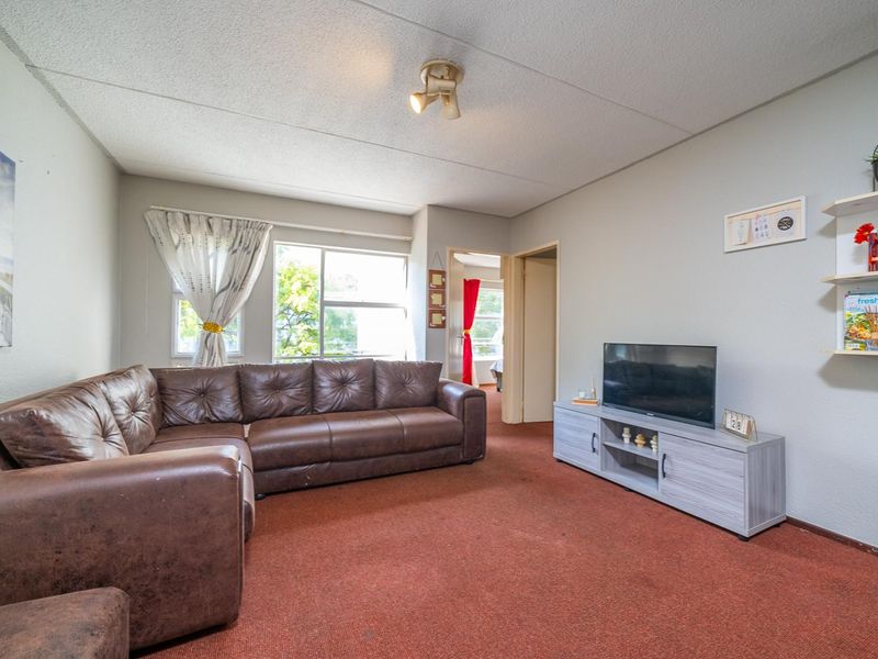 A living room featuring carpeted flooring, a ceiling-mounted spotlight, and an aluminium window frame, offering a functional space with potential for modernization.