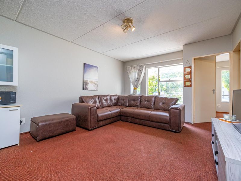 A living room featuring carpeted flooring, a built-in wall cabinet, and a window providing natural light.
