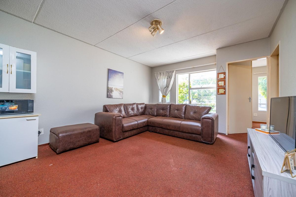 A living room featuring carpeted flooring, a built-in wall cabinet, and a window providing natural light.