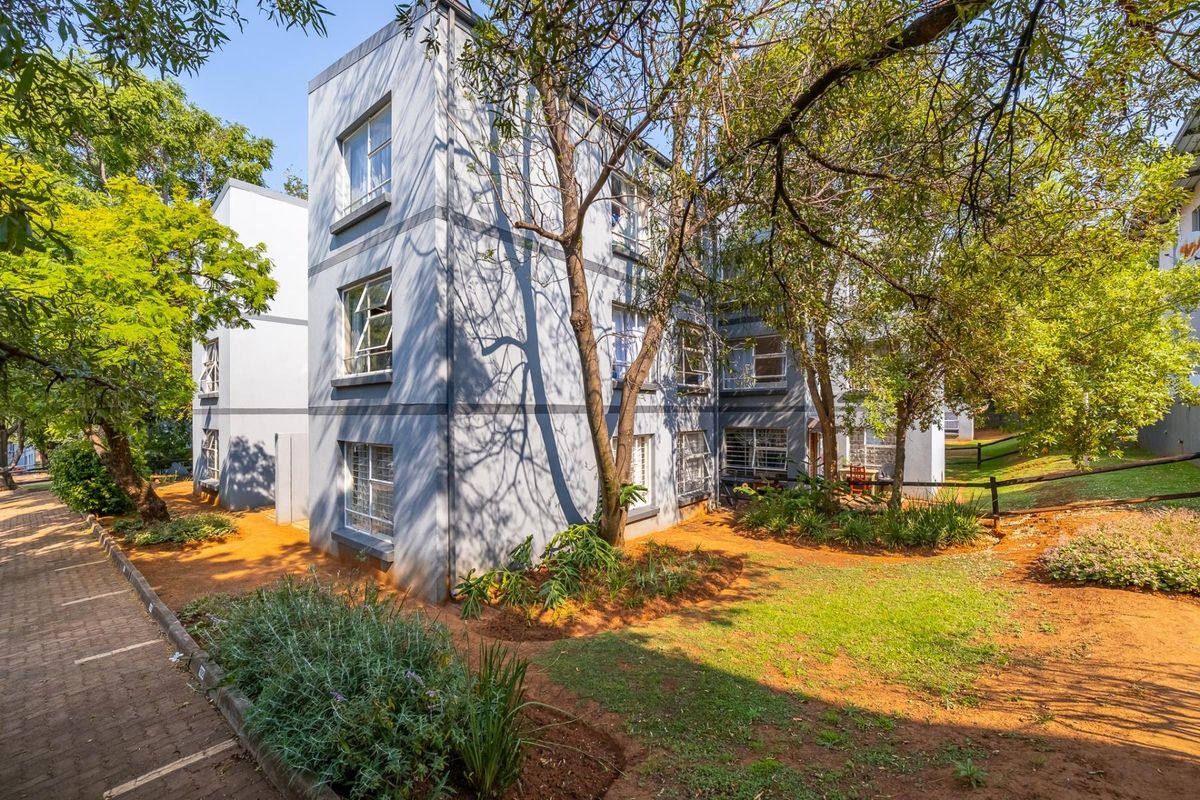 Exterior view of the apartment building featuring a paved walkway, landscaped garden area, and secure casement windows.