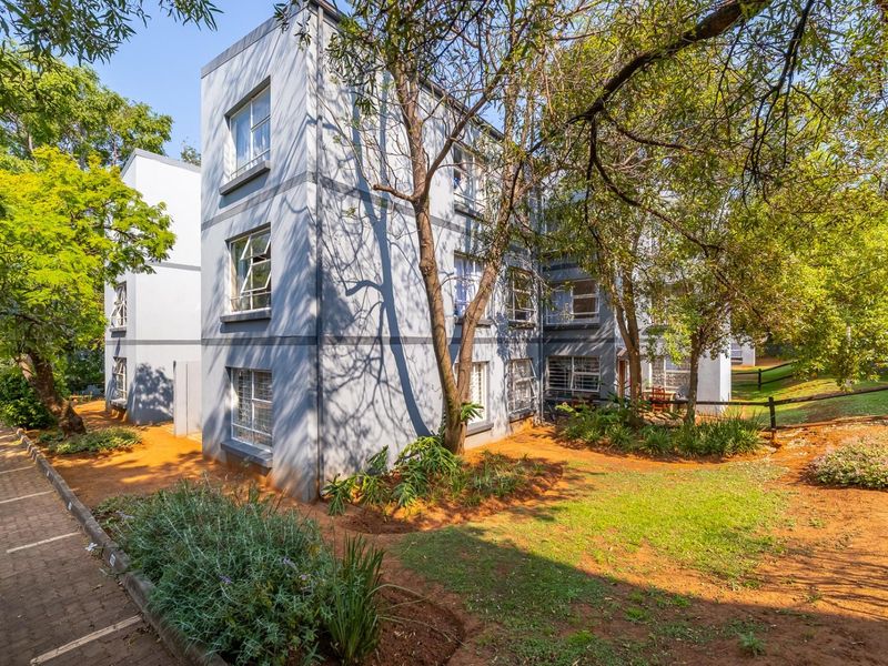 Exterior view of the apartment building featuring a paved walkway, landscaped garden area, and secure casement windows.