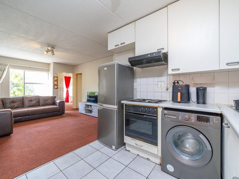 Open-plan living area and kitchen featuring built-in cabinetry, electric stove, extractor fan, and a combination of tiled and carpeted flooring.