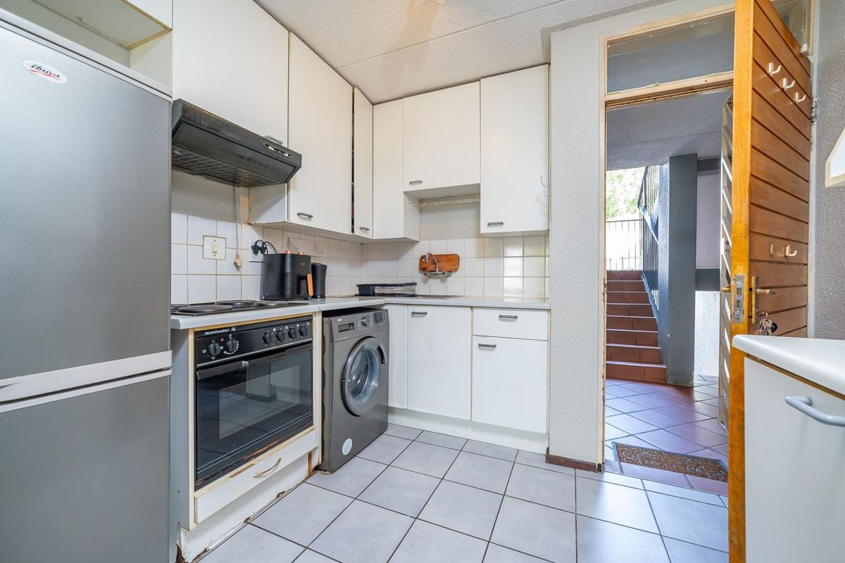 Compact kitchen featuring white cabinetry, tiled backsplash, built-in oven, hob, and integrated laundry plumbing, with direct access to the building stairwell.