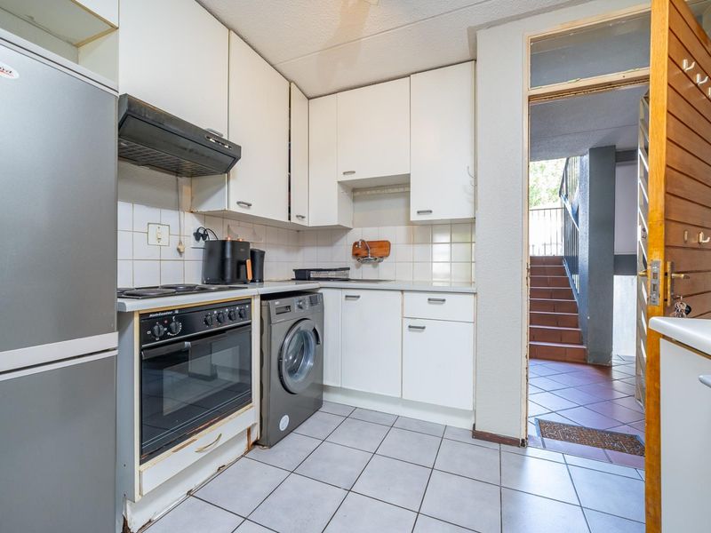Compact kitchen featuring white cabinetry, tiled backsplash, built-in oven, hob, and integrated laundry plumbing, with direct access to the building stairwell.