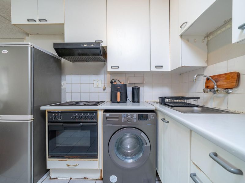 Compact kitchen featuring white cabinetry, tiled backsplash, built-in oven with hob, extractor fan, and integrated sink area.