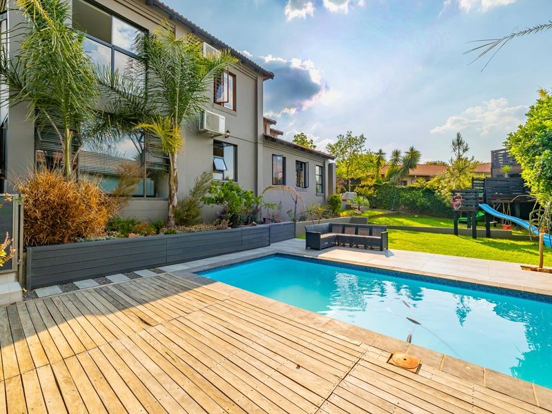A well-maintained outdoor pool area featuring timber decking, tiled patio space, and raised garden beds adjacent to the rear elevation of the house.