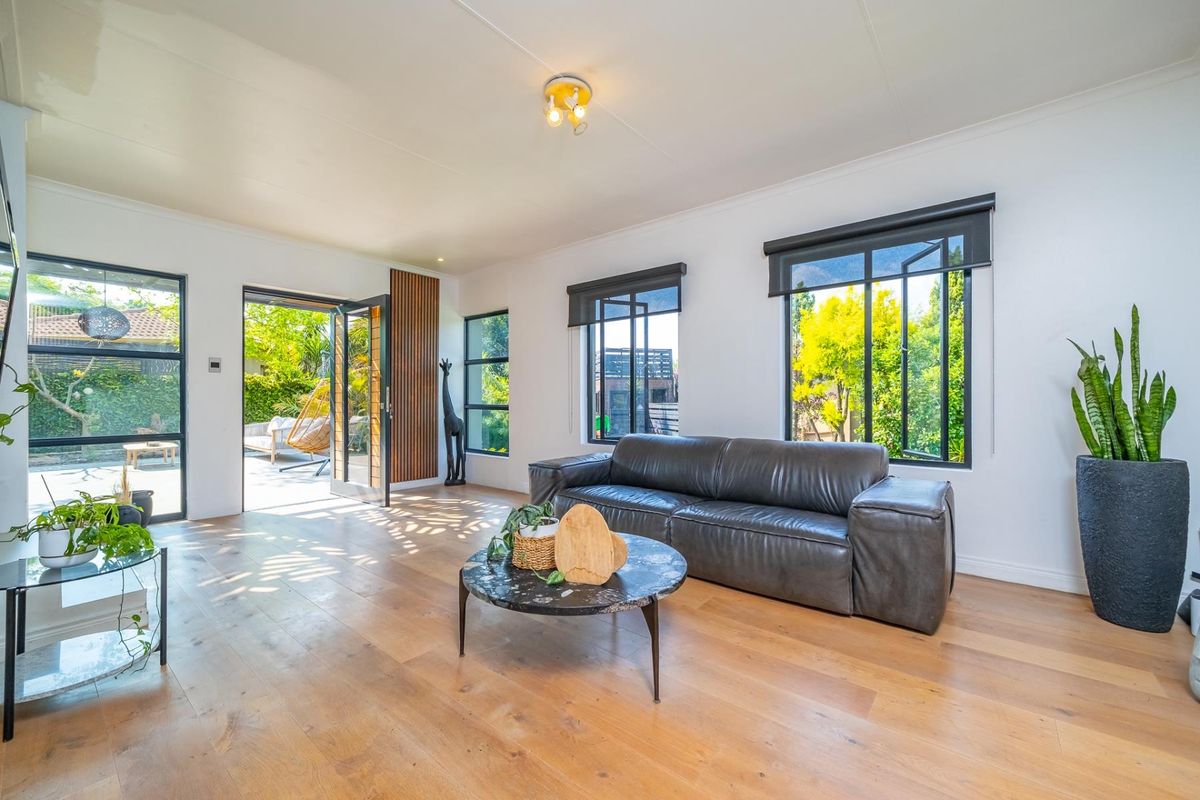 Bright and modern living room featuring hardwood flooring, large black-framed windows, and a stylish timber slat feature wall with direct access to the patio.