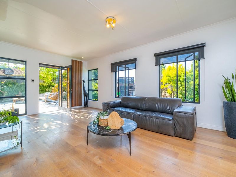 Bright and modern living room featuring hardwood flooring, large black-framed windows, and a stylish timber slat feature wall with direct access to the patio.