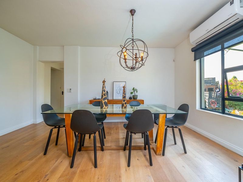 A bright dining room featuring light hardwood flooring, a modern metal pendant light, and a wall-mounted split-system air conditioner.