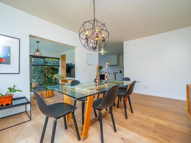 Bright open-plan dining area featuring hardwood flooring, modern pendant lighting, and seamless access to an adjacent living space and outdoor area.
