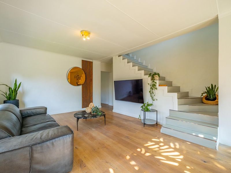 A bright living room featuring timber flooring, a modern staircase, and a wall-mounted television, creating a clean and contemporary living space.