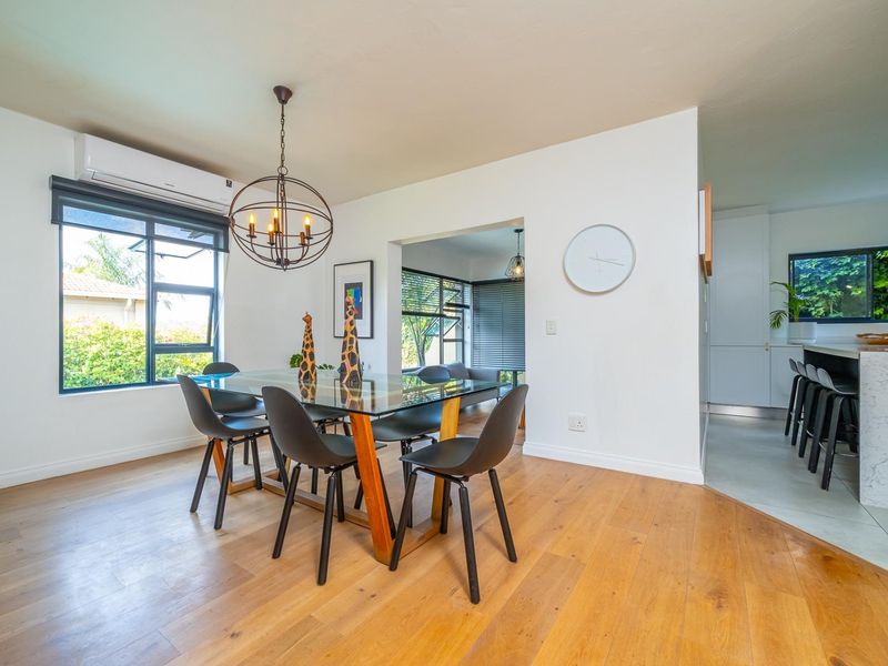 Bright open-plan dining area featuring timber flooring, split-system air conditioning, and a seamless transition to a modern kitchen with a stone island bench.