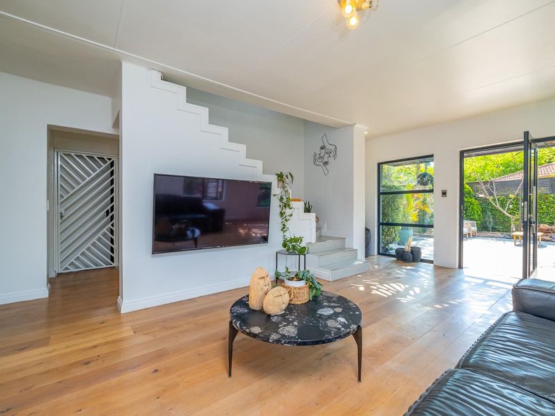 Bright living room featuring hardwood flooring, a modern staircase, and large black-framed glass doors providing seamless access to the outdoor patio area.