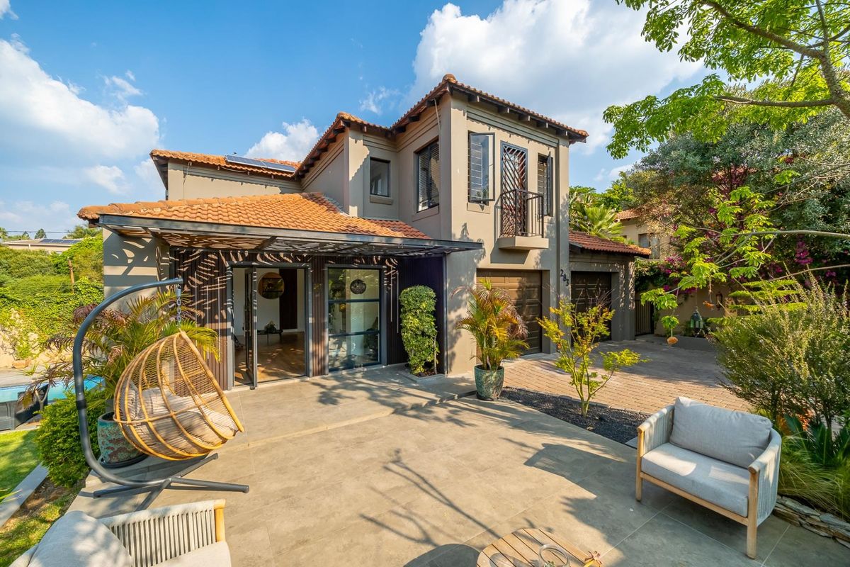 Rear view of a double-story residence featuring a paved patio, terracotta roof tiles, double garage, and a balcony overlooking the garden.