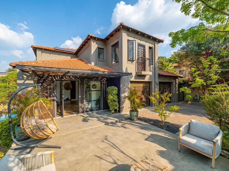 Rear view of a double-story residence featuring a paved patio, terracotta roof tiles, double garage, and a balcony overlooking the garden.