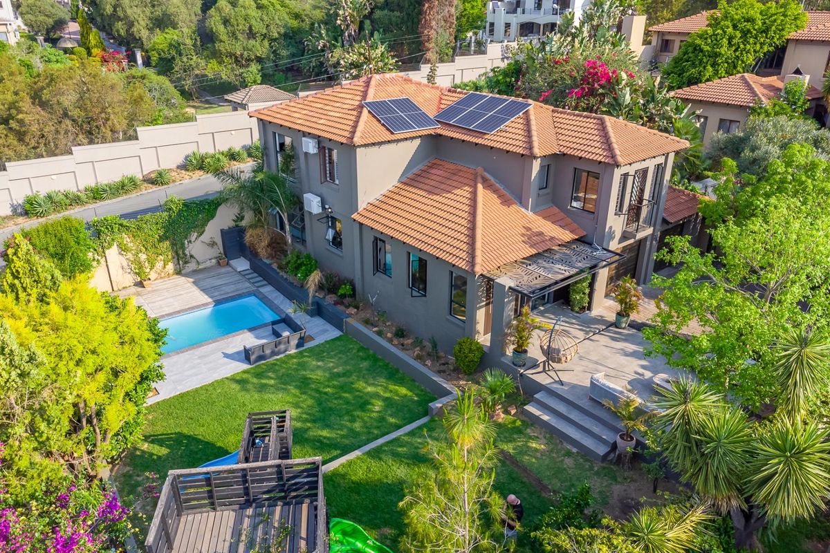 Aerial view of a two-story residential property featuring a tiled roof with solar panels, a swimming pool, landscaped garden, and a paved patio area.