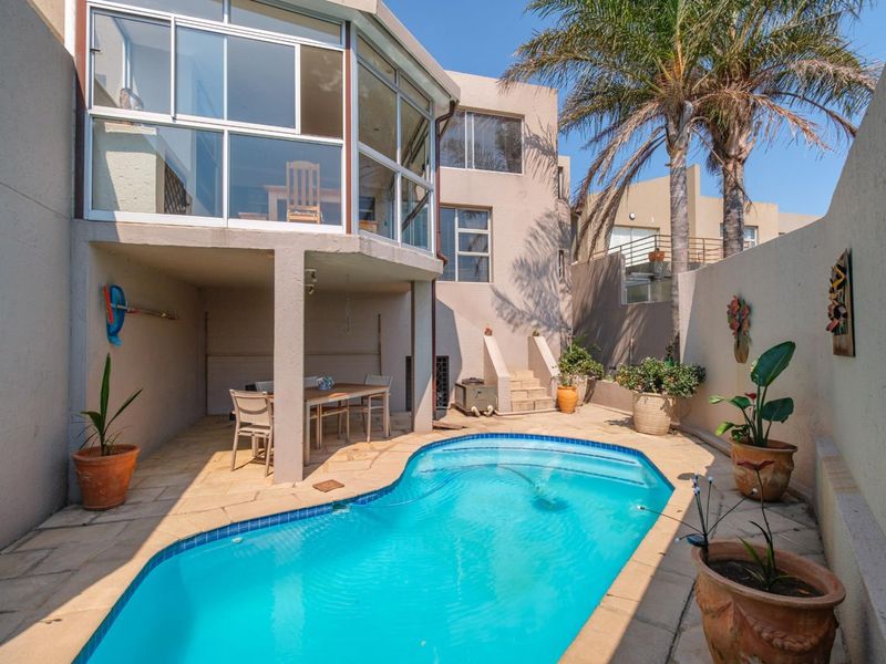 Private courtyard featuring a swimming pool and a covered patio area, overlooked by a multi-level townhouse facade with large windows.