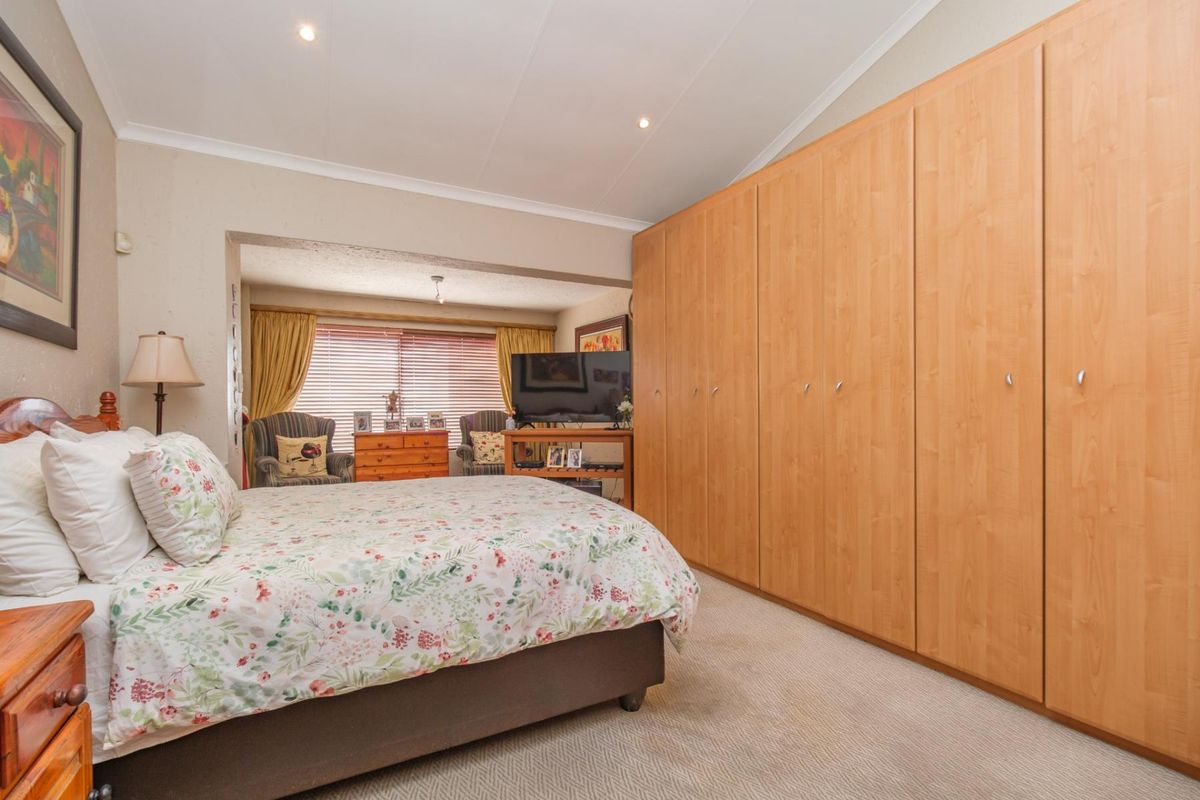 Spacious bedroom featuring extensive built-in wooden cabinetry, neutral carpeting, and recessed lighting, with an adjoining seating area by the window.