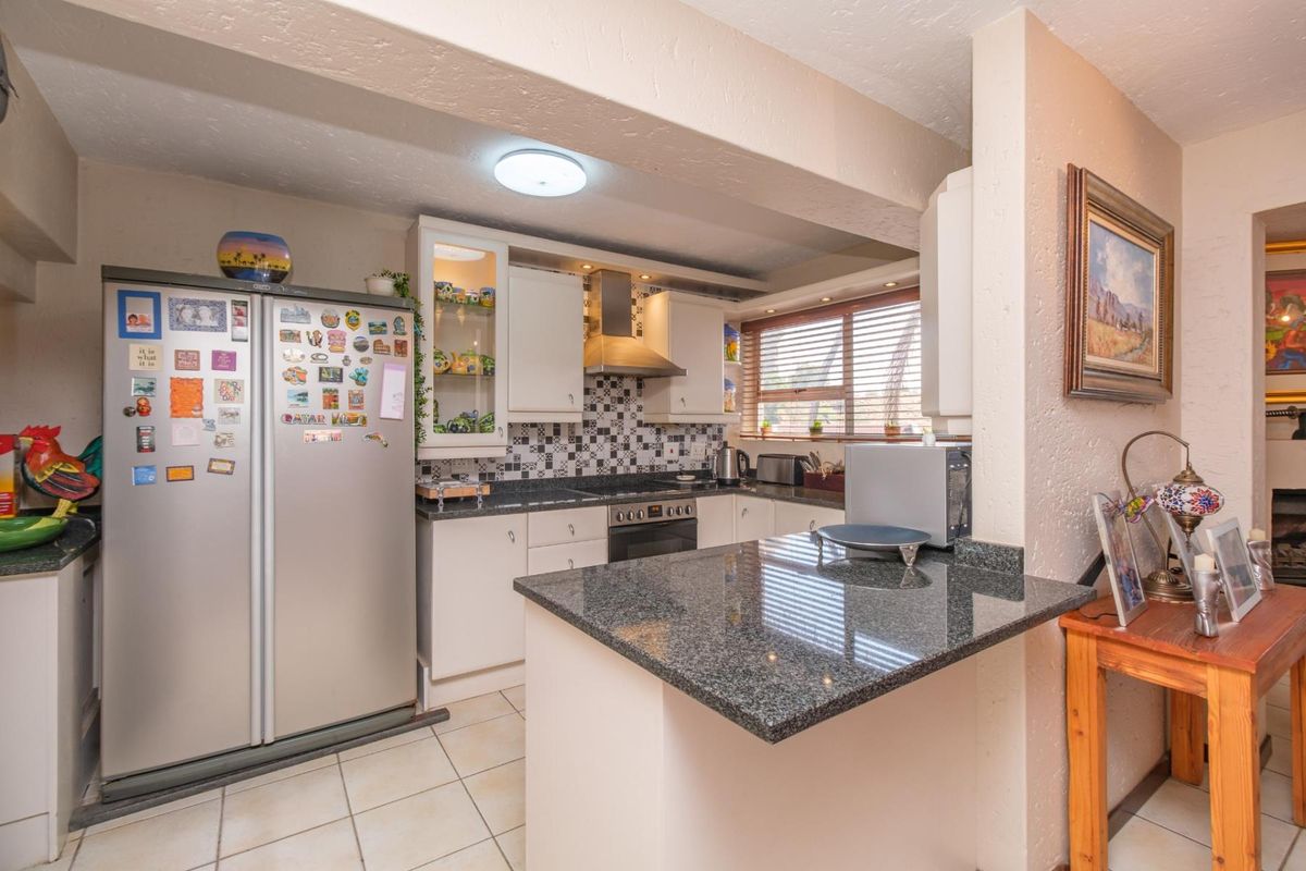 A functional kitchen featuring granite countertops, built-in oven with extractor fan, tiled flooring, and a breakfast bar, offering a practical layout for daily use.