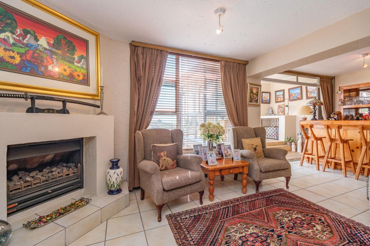 A cozy living room featuring a built-in fireplace, tiled flooring, and large windows with blinds, offering a warm and inviting atmosphere.
