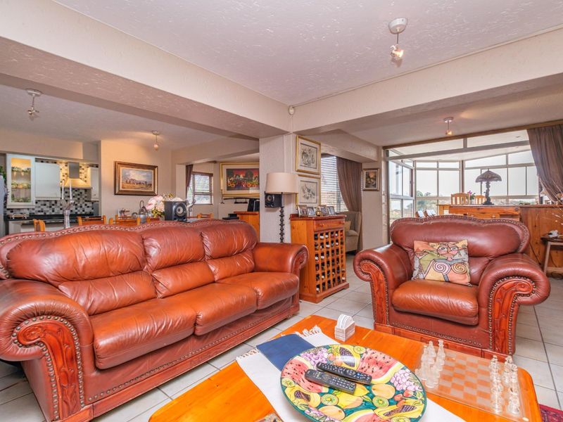 Spacious open-plan living area featuring tiled floors, integrated kitchen space, and a bright sunroom enclosure with large windows.