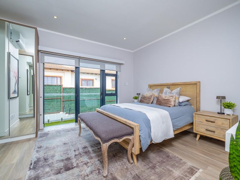 Modern bedroom featuring laminate flooring, built-in mirrored cupboards, and a sliding glass door providing access to the exterior.