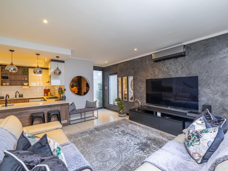 Modern open-plan living area featuring a contemporary kitchen with stone countertops, integrated appliances, and a stylish textured feature wall with air conditioning.