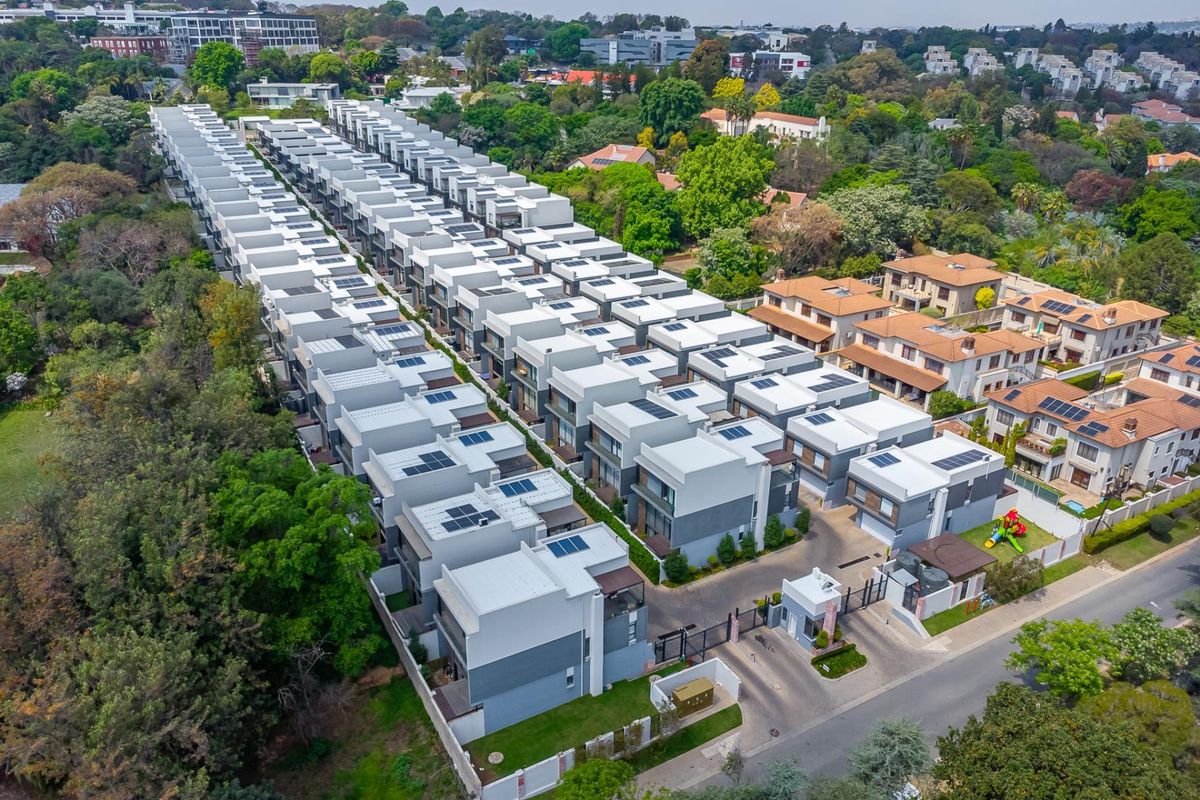 Aerial view of a modern residential townhouse complex featuring uniform architecture, solar panels, and a secure gated entrance.