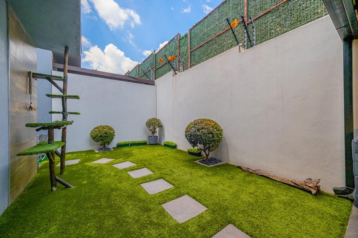 A private rear courtyard featuring artificial turf, stone pavers, and high perimeter walls secured with electric fencing.