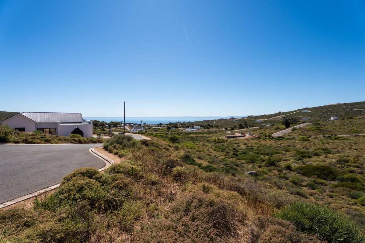 A scenic view overlooking the vacant residential land, featuring natural coastal vegetation, paved road access, and distant ocean views.