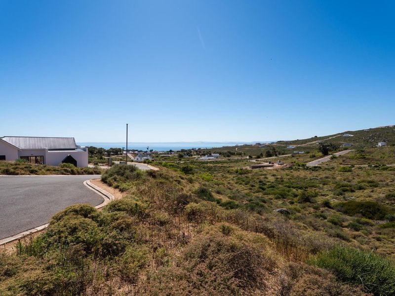 A scenic view overlooking the vacant residential land, featuring natural coastal vegetation, paved road access, and distant ocean views.
