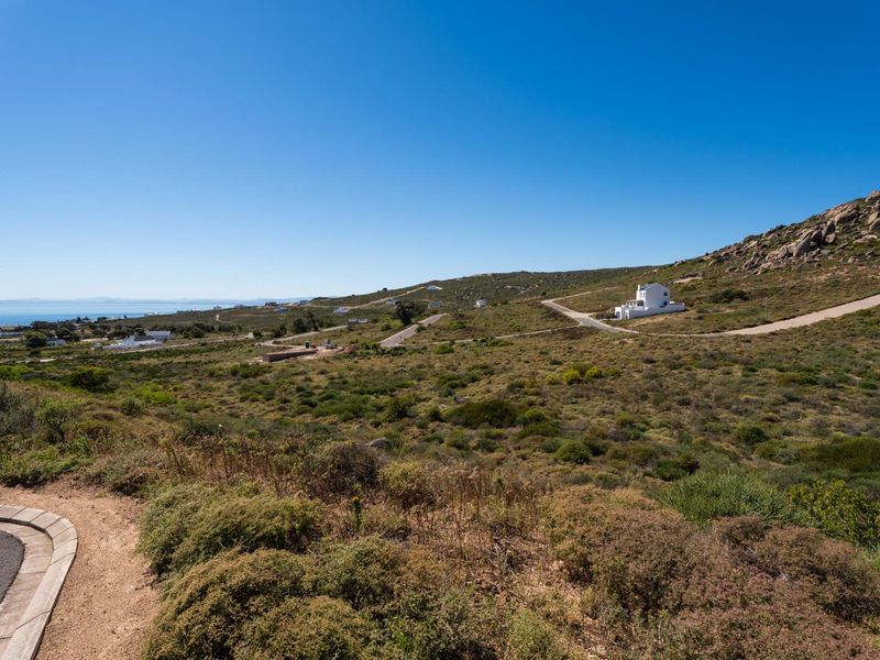 A wide-angle view of the vacant residential land, featuring natural coastal landscape, surrounding hills, and existing paved road infrastructure.