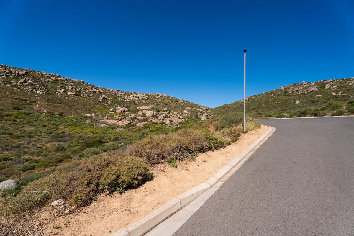 A view of a paved residential street with concrete curbing and a street light, bordering natural rocky hillside terrain.
