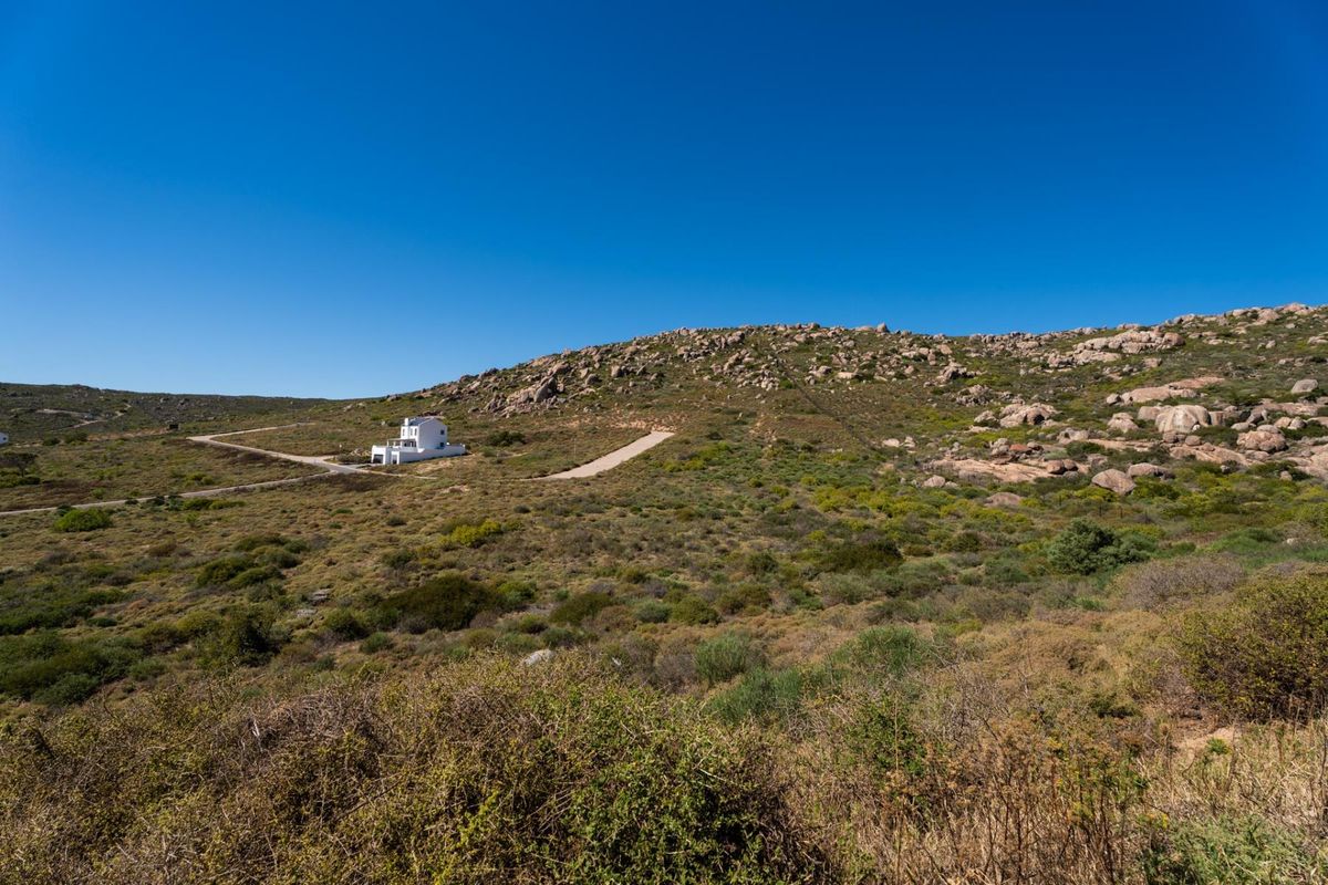 An aerial view of a large vacant residential plot featuring natural rocky landscape and a gravel access road leading to a distant property.