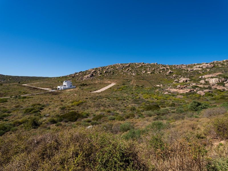 An aerial view of a large vacant residential plot featuring natural rocky landscape and a gravel access road leading to a distant property.