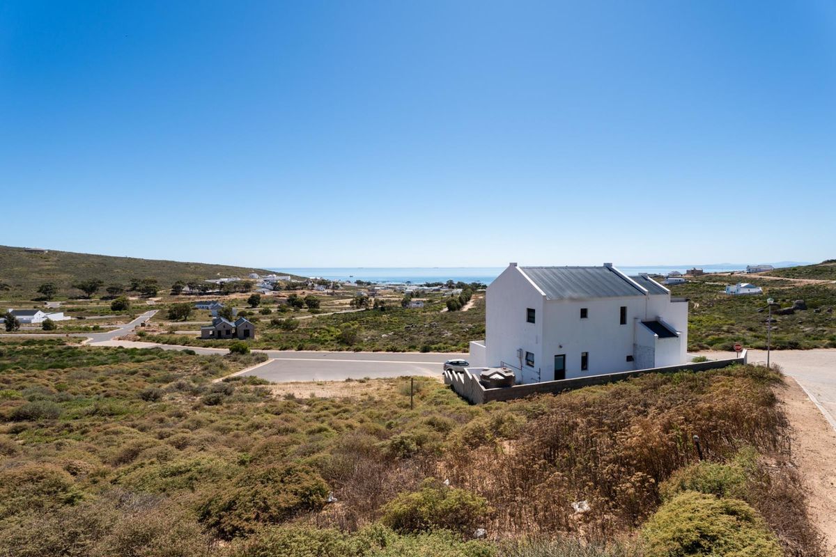 An elevated aerial view of a residential property featuring a white house with a metal roof, situated in a coastal landscape.