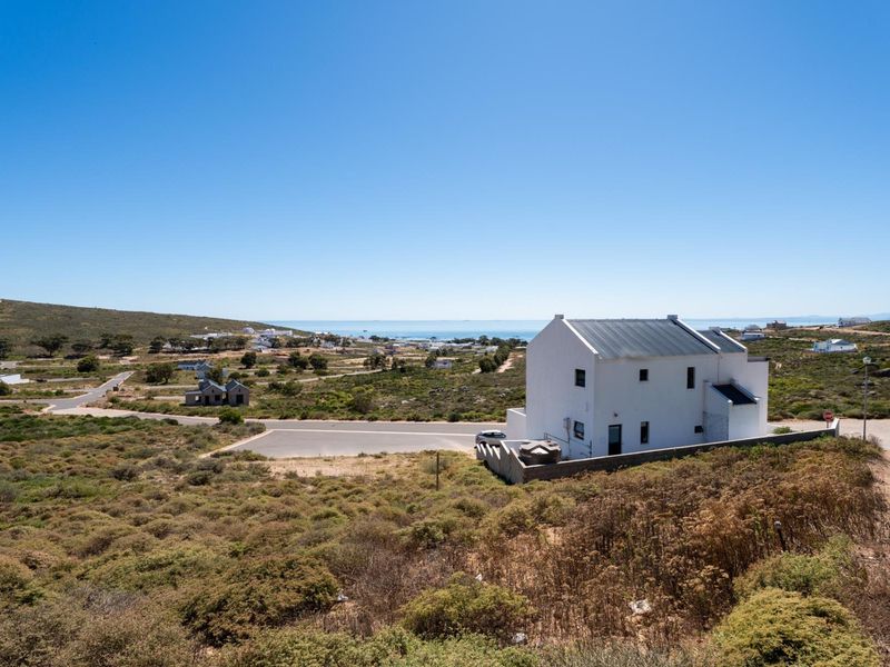 An elevated aerial view of a residential property featuring a white house with a metal roof, situated in a coastal landscape.