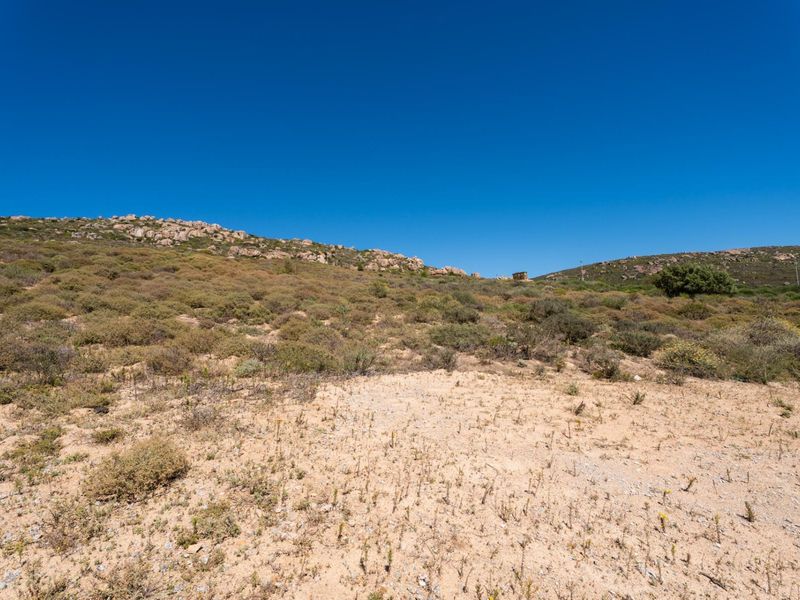 A view of the vacant residential land featuring natural rocky terrain and native vegetation under a clear blue sky.