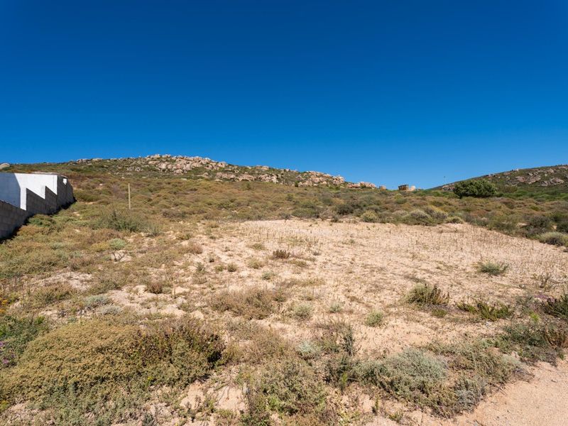 A vacant residential plot featuring natural vegetation, rocky terrain, and a partial boundary wall, offering potential for development in a scenic landscape.