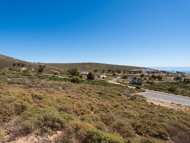 A wide-angle view of the coastal residential landscape, featuring natural vegetation, paved road infrastructure, and distant ocean views.