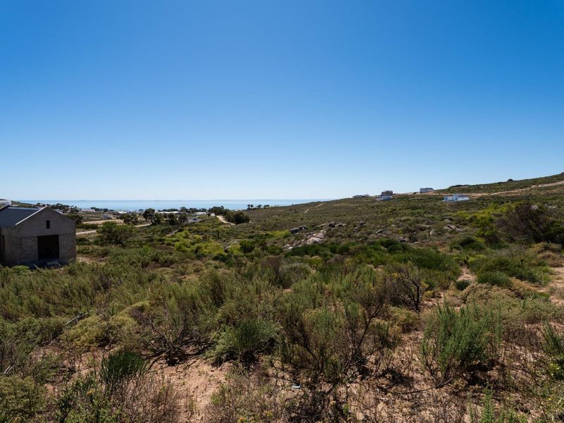 A wide-angle view of a vacant residential plot featuring natural coastal vegetation and distant ocean views.