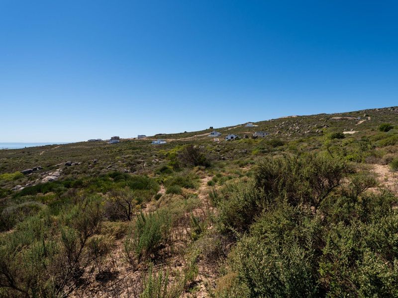 A wide-angle view of the vacant residential land featuring natural coastal vegetation and distant ocean views.