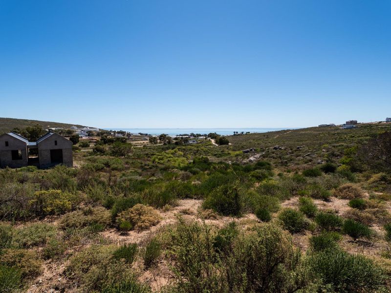 A wide-angle view of a coastal residential plot featuring natural fynbos vegetation and distant ocean views.