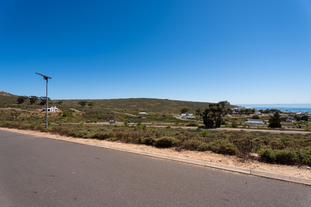 A wide-angle view of the vacant residential land, featuring paved road access, a solar street light, and scenic coastal landscape views.