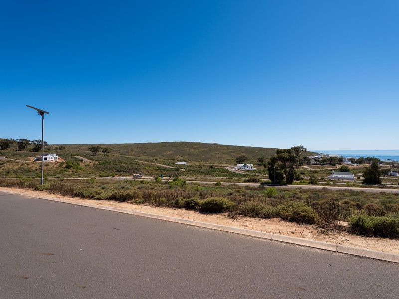 A wide-angle view of the vacant residential land, featuring paved road access, a solar street light, and scenic coastal landscape views.