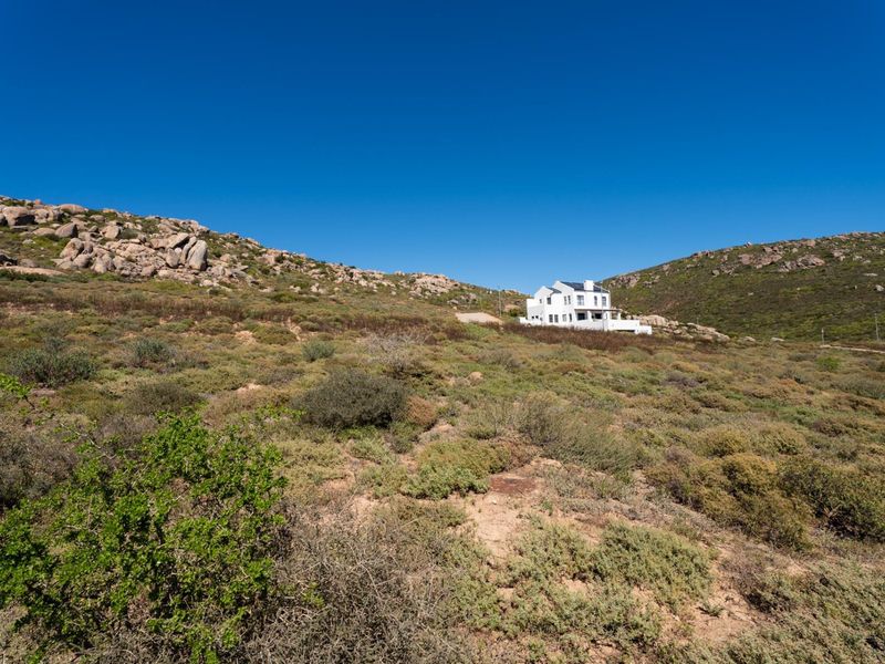 A wide-angle view of the vacant residential land featuring natural rocky terrain and native vegetation with a distant house visible.