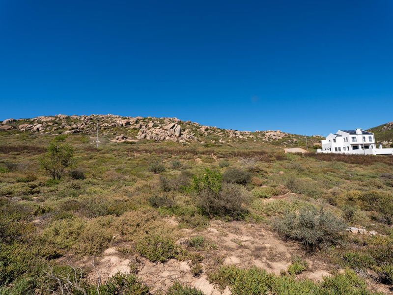 A wide-angle view of the vacant residential land featuring natural rocky terrain and native coastal vegetation under a clear blue sky.