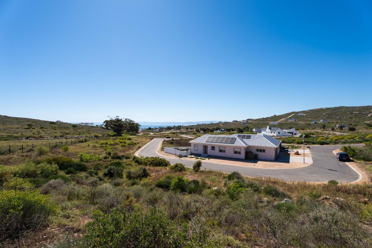 Aerial view of a residential property featuring a house with solar panels, situated in a coastal landscape with surrounding natural vegetation.