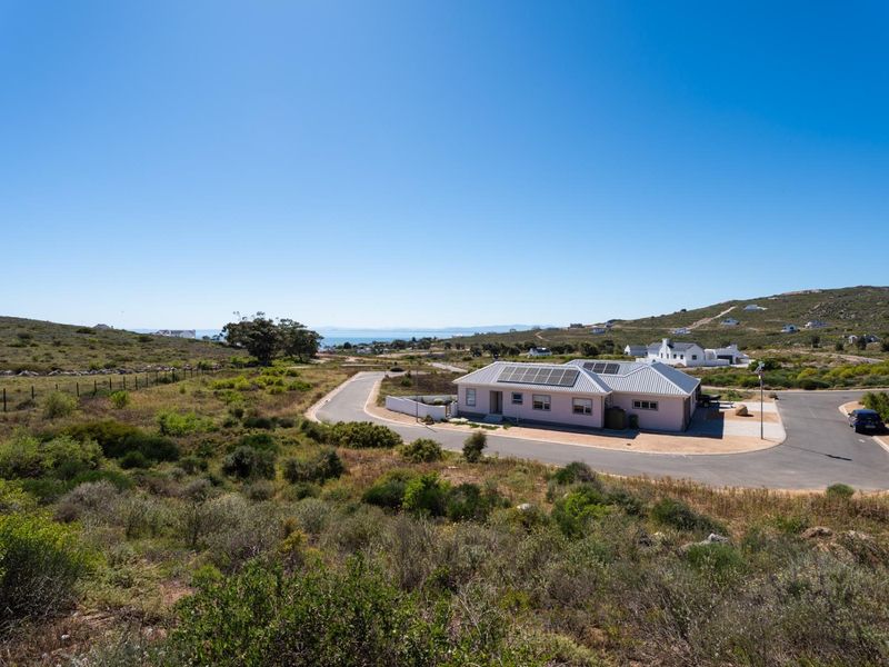 Aerial view of a residential property featuring a house with solar panels, situated in a coastal landscape with surrounding natural vegetation.