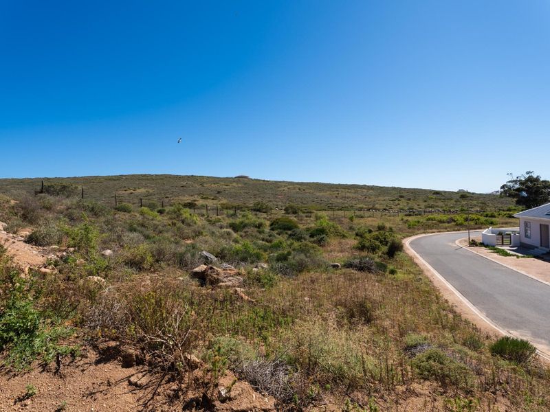 An elevated view of the vacant residential land, featuring natural coastal vegetation, perimeter fencing, and adjacent paved road access.